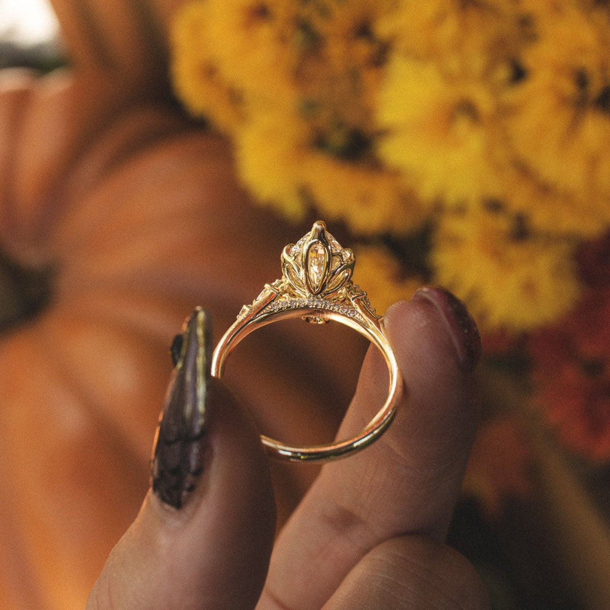 Made-to-order Jillian marquise lab grown diamond engagement ring in yellow gold, held in hand against fall flowers