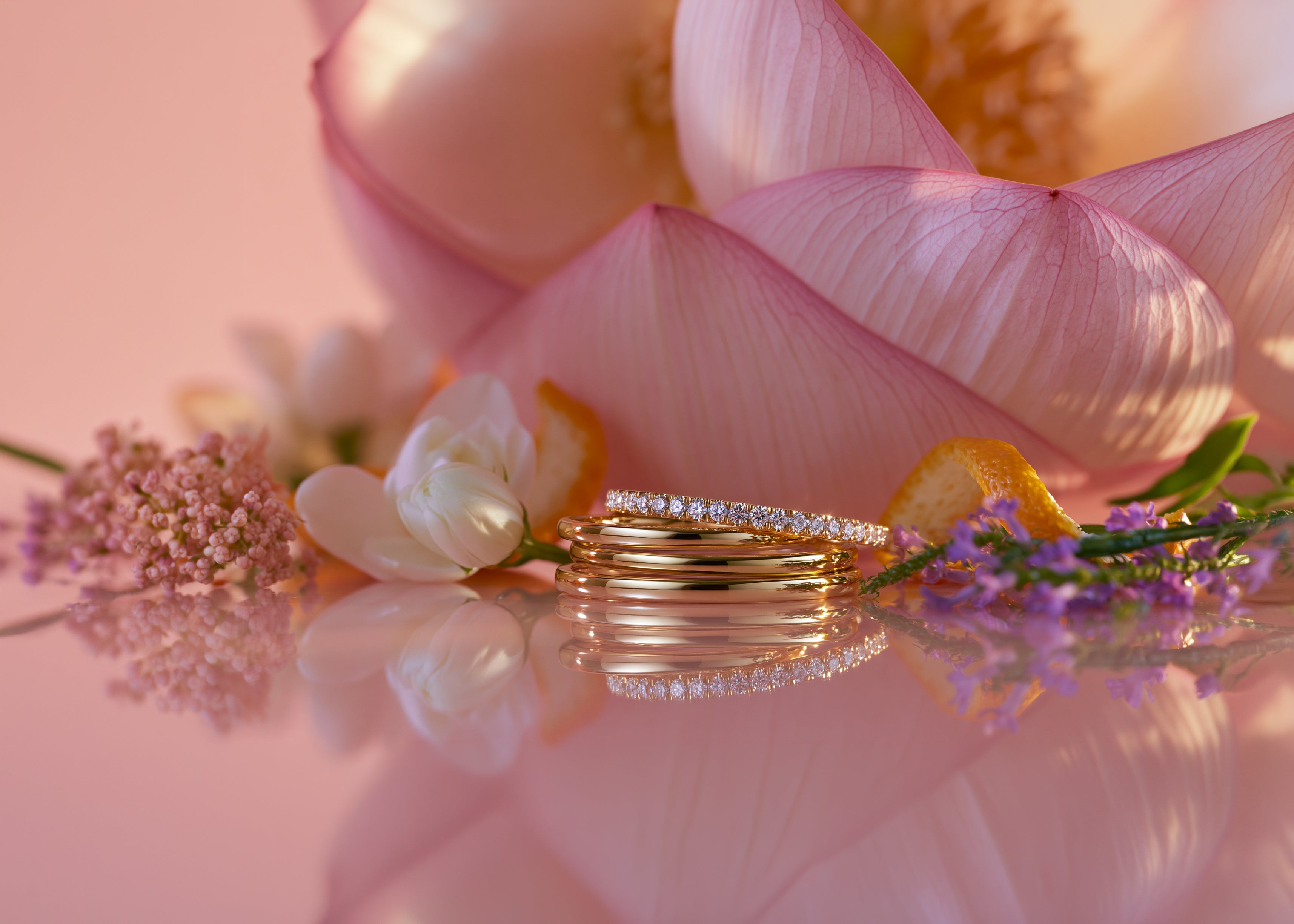 Gold rings on a reflective surface with pink lotus flowers in the background