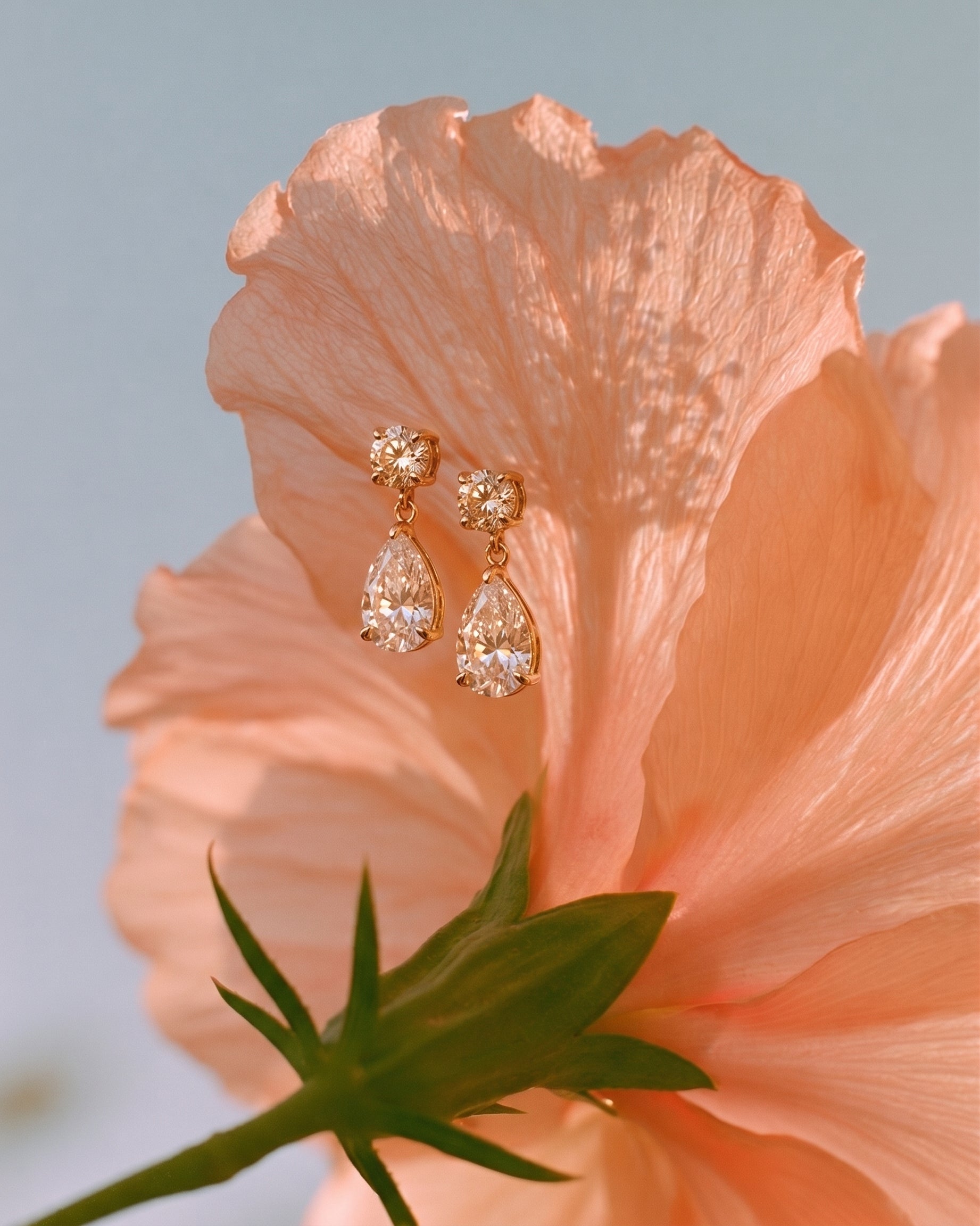 Rose gold teardrop earrings on a peach-colored flower with a soft focus background