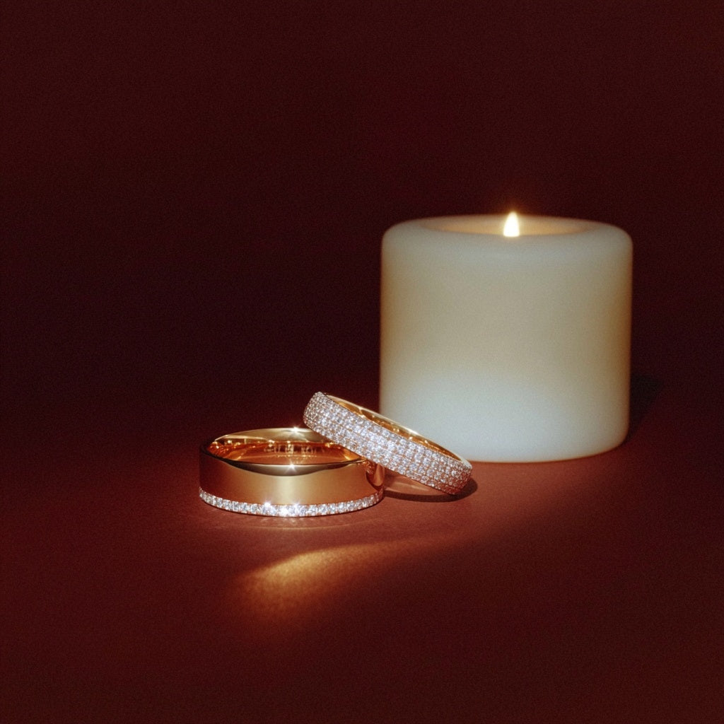 Two gold rings with diamond accents next to a lit candle on a dark background