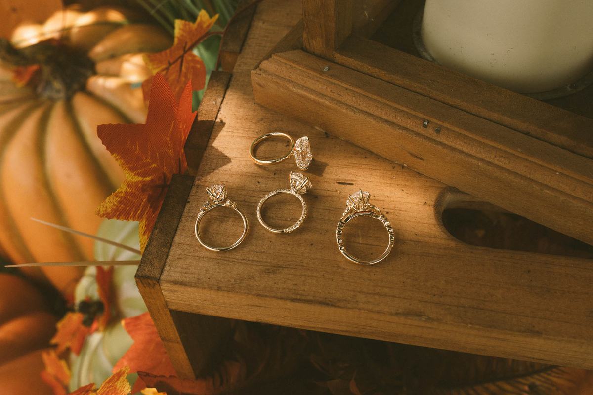Custom lab grown diamond engagement rings in yellow gold on a rustic wood table with fall leaves