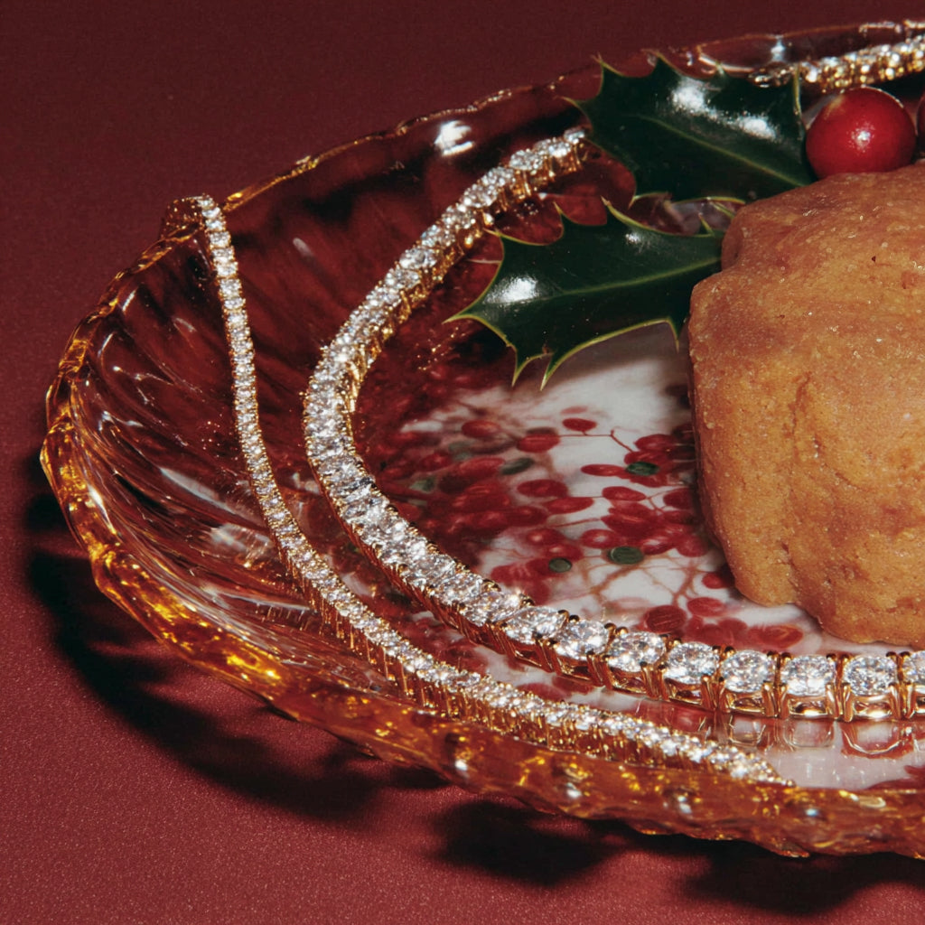 diamond tennis bracelets on a cranberry christmas bowl next to holly and holiday cake