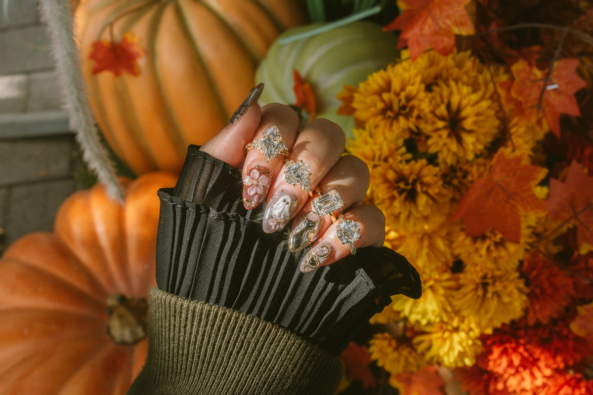 Hand with fall nail art wearing lab grown diamond engagement rings against autumn pumpkins and flowers