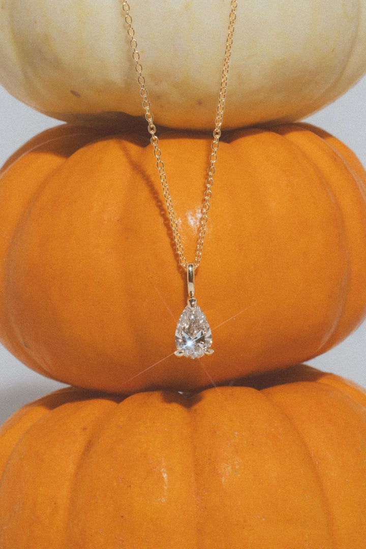 Pear lab grown diamond solitaire necklace in yellow gold on stacked pumpkins