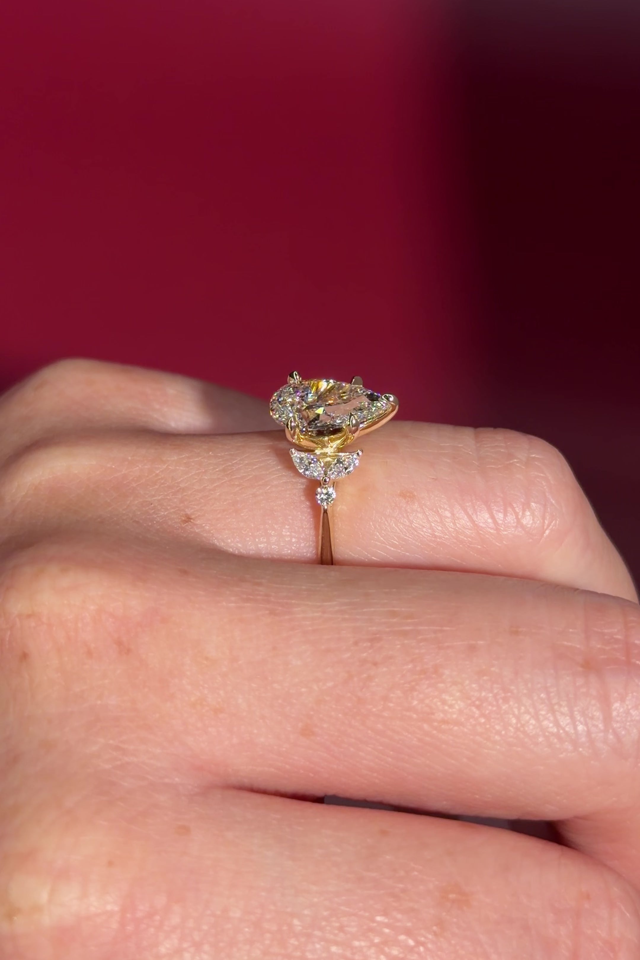 2.01ct F-VVS2 Pear Lab Diamond Sarah. The Sarah features a tapered high polish comfort fit band with a trio of diamonds. The trio features two marquises and one round diamond. The baskets are all lifted to fit a straight band flush against the body.